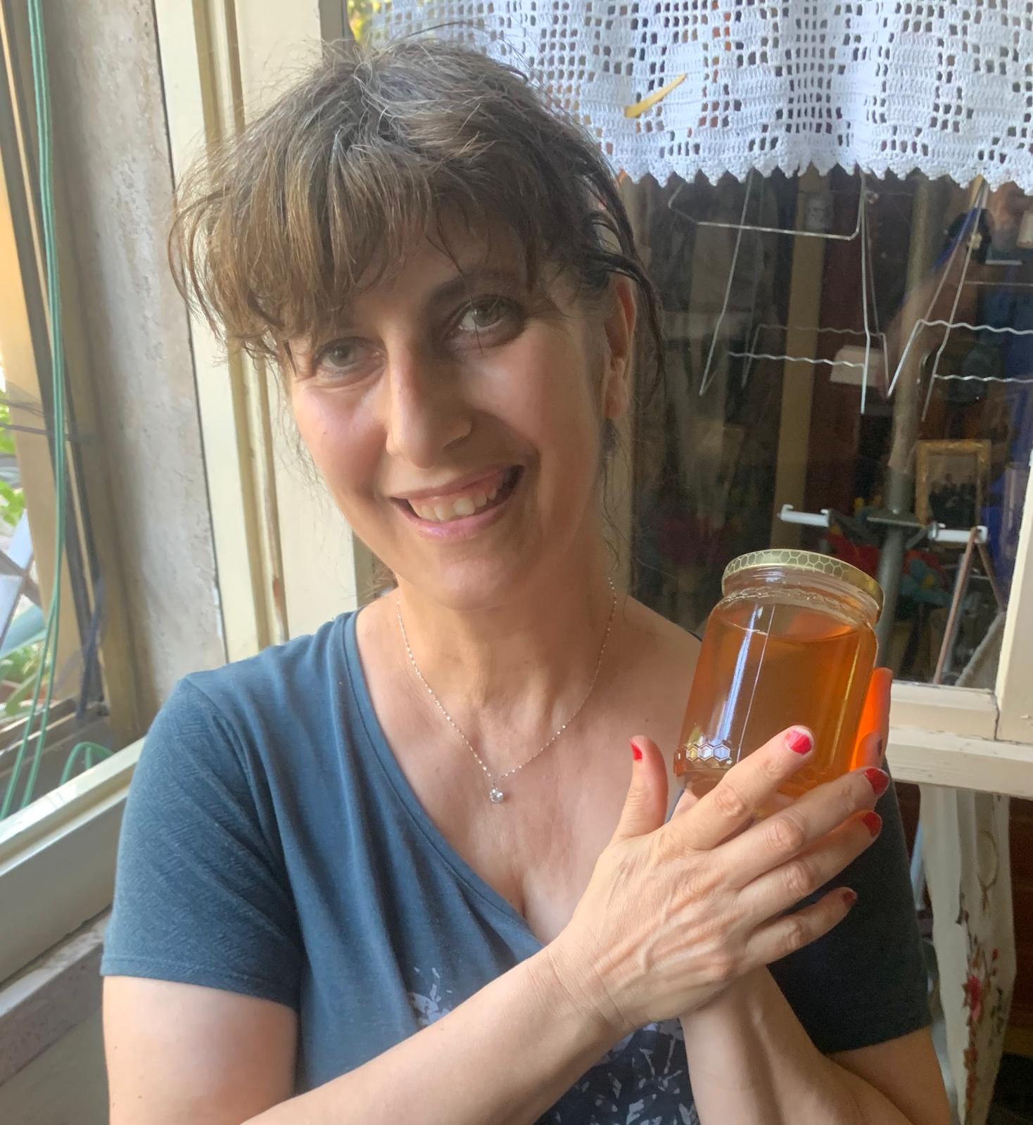 Mimi sorride tenendo tra le mani un vasetto del suo miele